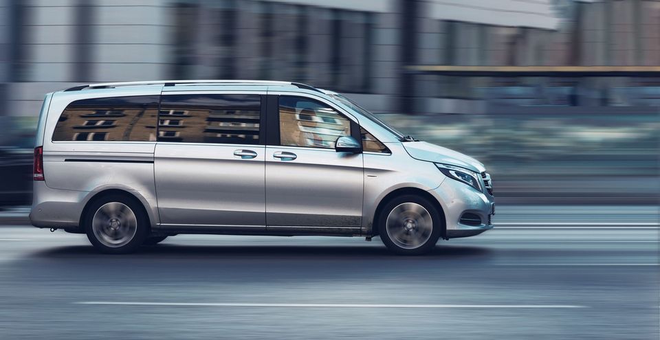 A silver minivan is driving quickly on an urban street with motion blur indicating speed.